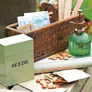 Boxes and packets of seeds on a table top next to a wooden box and a green water spray