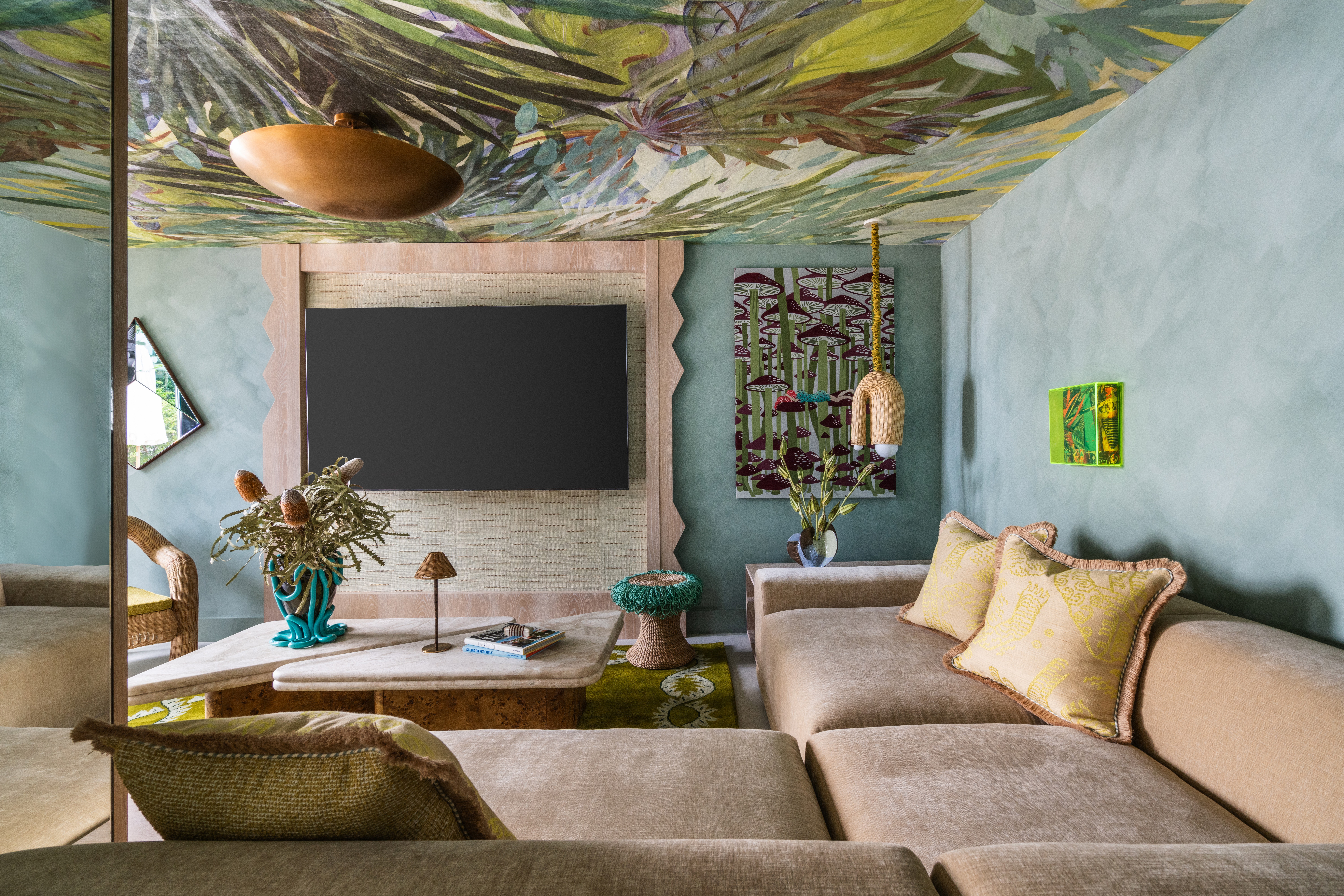 Interior of a tropical home with teal walls, zellige tiles surfaces, wavy, sand-coated details, rattan furniture mixed with bright aquamarine and ochre touches, and a botanical-themed mural ceiling.
