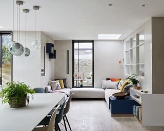 A kitchen extension with a dining table under pendant lighting next to a living space with a large window