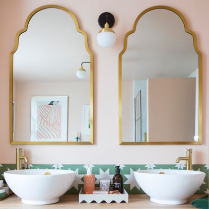 a bathroom with a large vanity unit, twin mirrors and twin basins with pale pink walls and a tiled green and white star print splashback