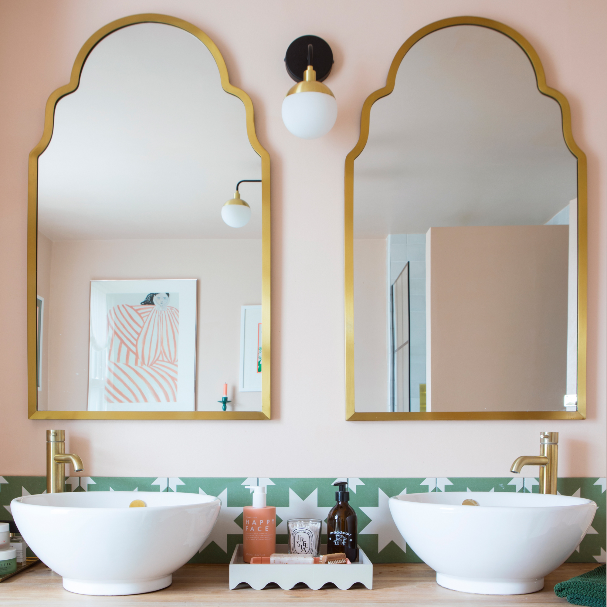 a bathroom with a large vanity unit, twin mirrors and twin basins with pale pink walls and a tiled green and white star print splashback