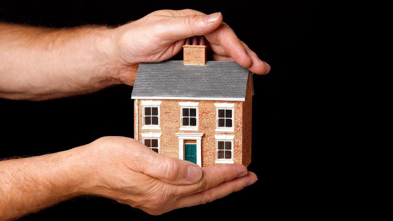 Pair of hands holding a small model of a home on a black background