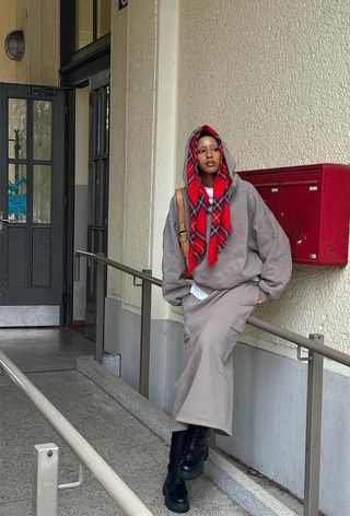 A woman outside wearing a gray hoodie with a white t-shirt, a gray cargo skirt, and black combat boots.