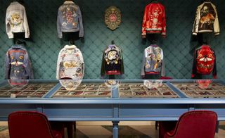 Jackets with various types of patches on them hanging on a wall in front of a glass display case with many different types of patches for the jackets inside of it.