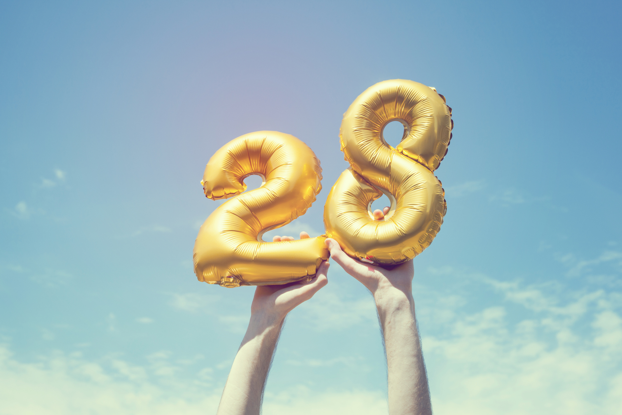  two arms holding up the number "28" against a blue sky 