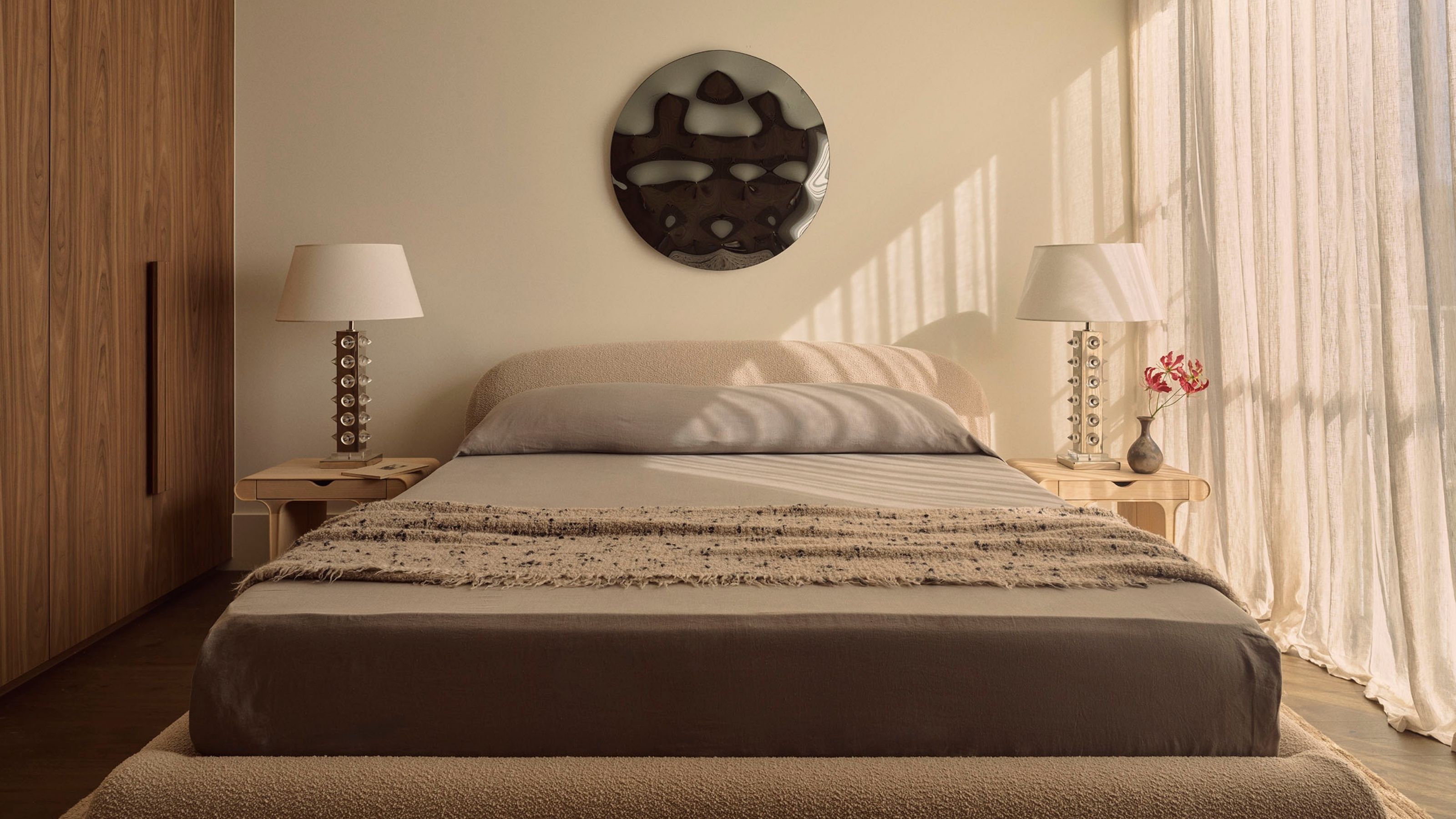 Image of a neutral, cozy bedroom with textured bedding and curtains over the window on the right wall.
