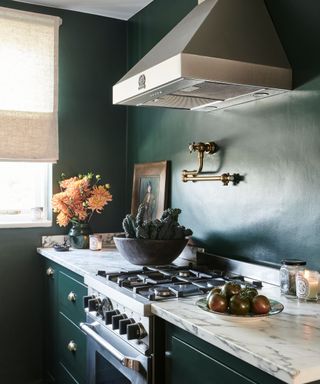 A dark green kitchen with marble countertops and gold hardware