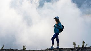 View of woman in activewear standing on a hill with backpack