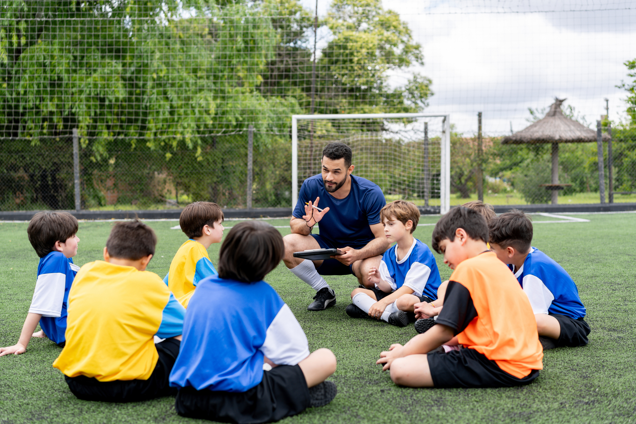 A soccer coach talking to a group of kids training in the field.
