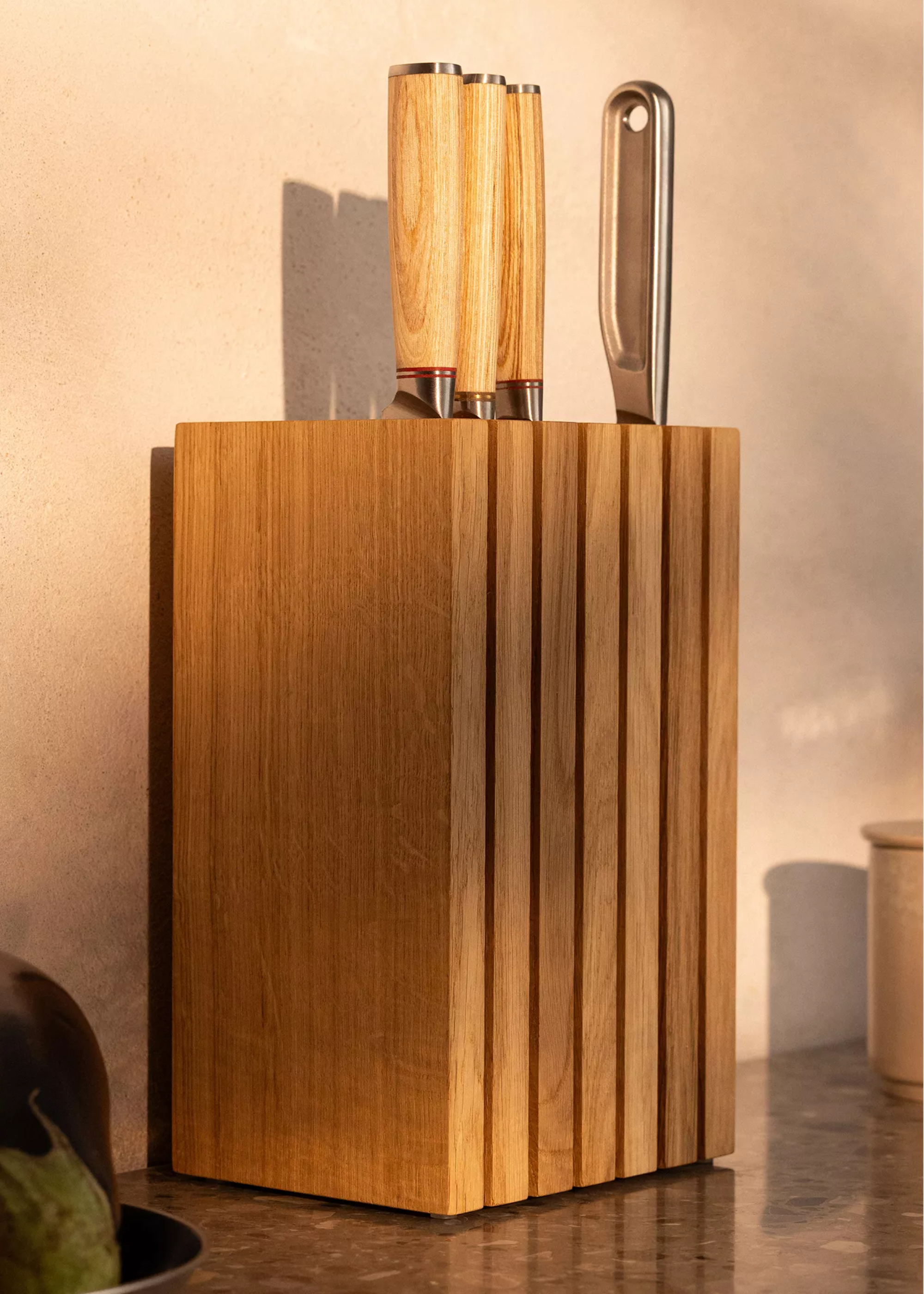 A wood knife block against a sunlit wall on a stone countertop