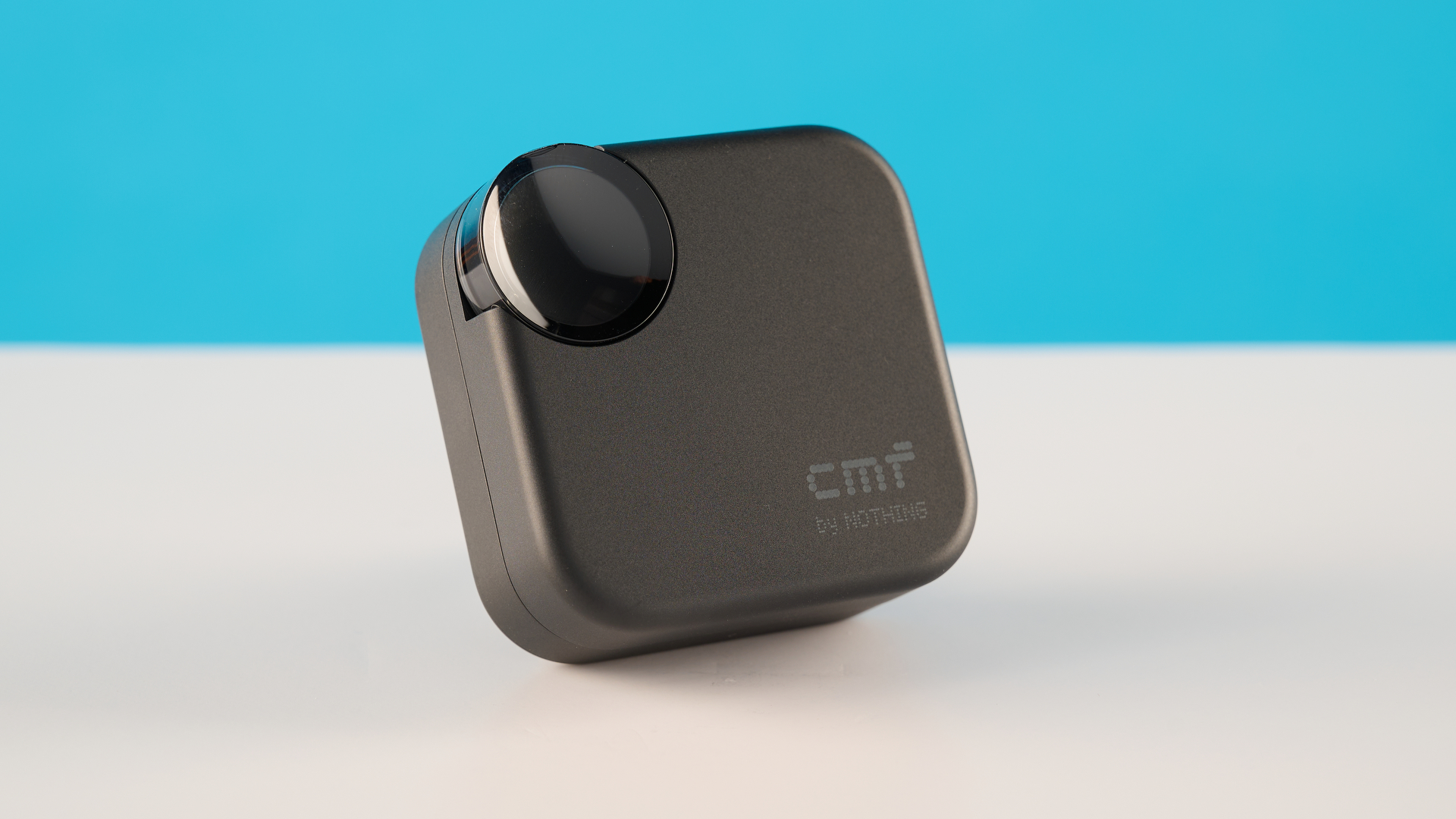 CMF Buds 2 in Dark Gray photographones on a gray table in front of a blue background