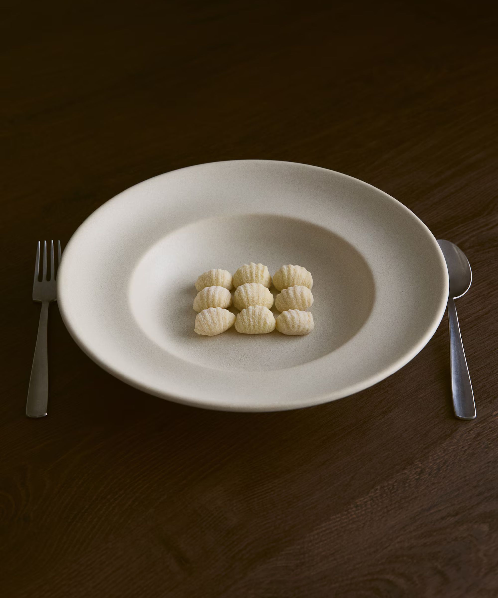 white bowl plate with ravioli with silver cutlery on dark timber table