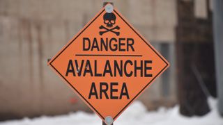 photo of a diamond-shaped orange sign that reads "danger, avalanche area" with a skull and cross bones at the top