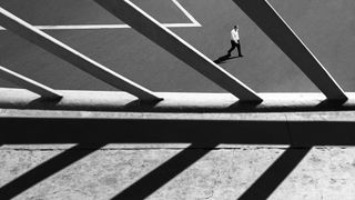 Person walking in a parking lot with diagonal shadows from overhead structure