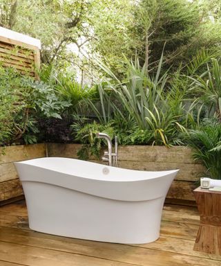 white bath with shower on a wooden deck pation surrounded by tropical plants