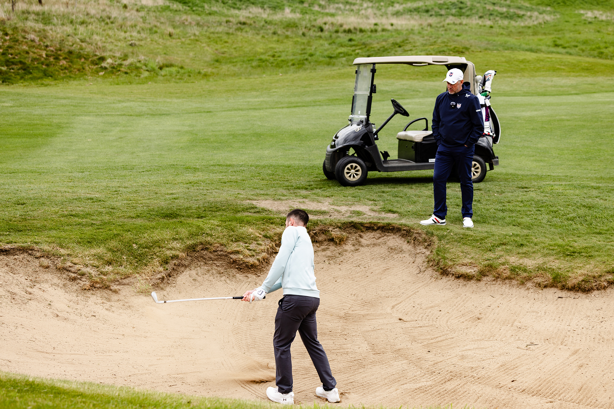 Lee Westwood watching Baz Plummer hit a bunker shot before giving him tips on how to improve out of the sand