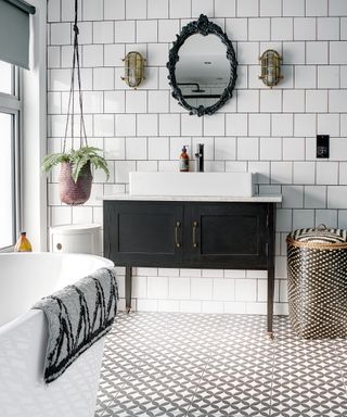 Bathroom with white tile wall and bath, grey and white geometric tile floor, black and white sink, and colourful decorative touches.