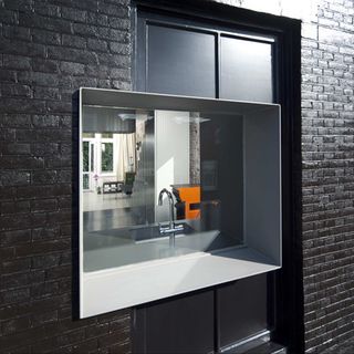 An upclose view of the black brick building with a view of the glass window with grey panels that shows a peek of the interior