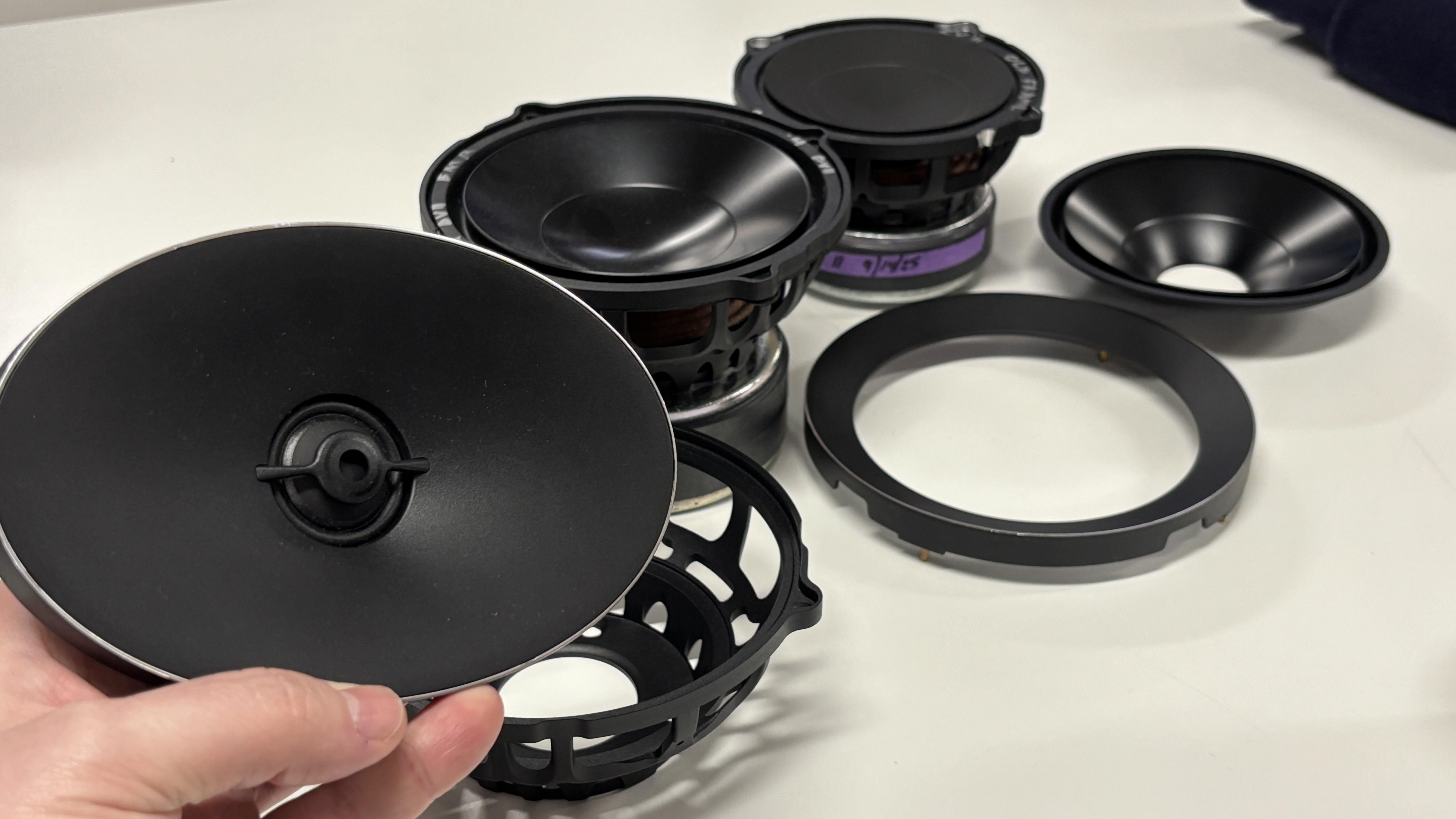 Arcam Radia R45 driver units laid out on a table with the tweeter and waveguide being held in a man's hand