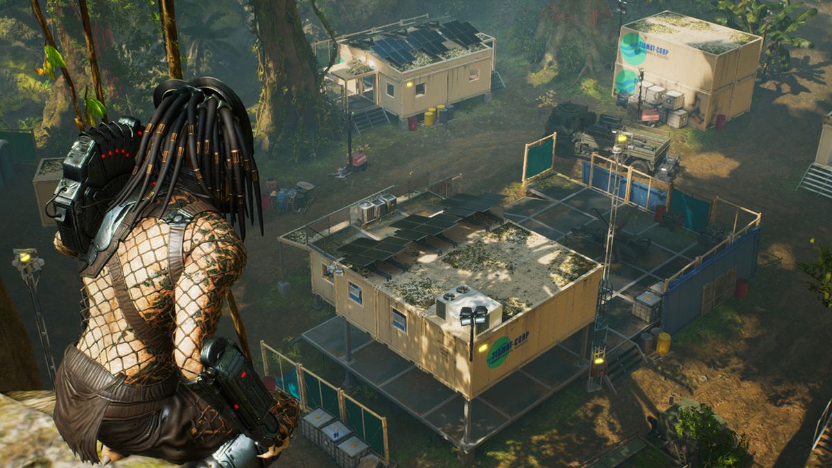 A dreadlocked alien kneeling on a cliff face looking down on a facility comprised of three buildings in the jungle.