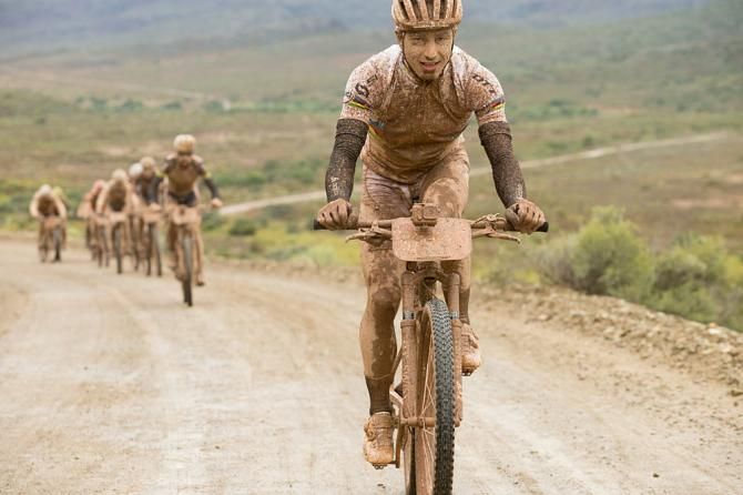 A muddy, smiling Nino Schurter of team Scott-Odlo MTB racing leads a bunch up a climb during stage 2