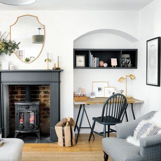 Grey and white study room with bookcase and desk in alcoves either side of fireplace with wood burner and unusual shaped mirror above