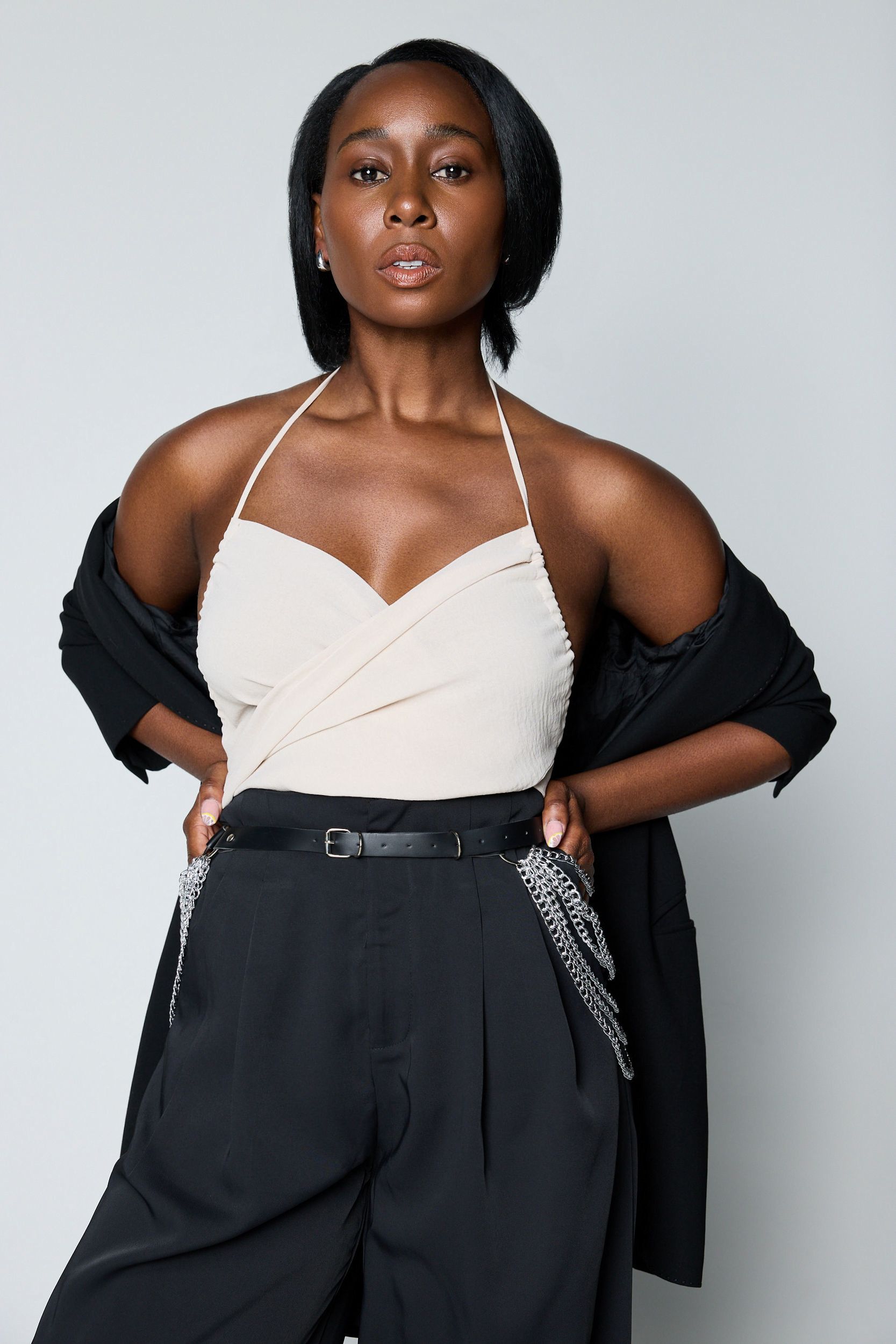 actress sasha compere wears a white tank top and black trousers posing with her hands on her hips