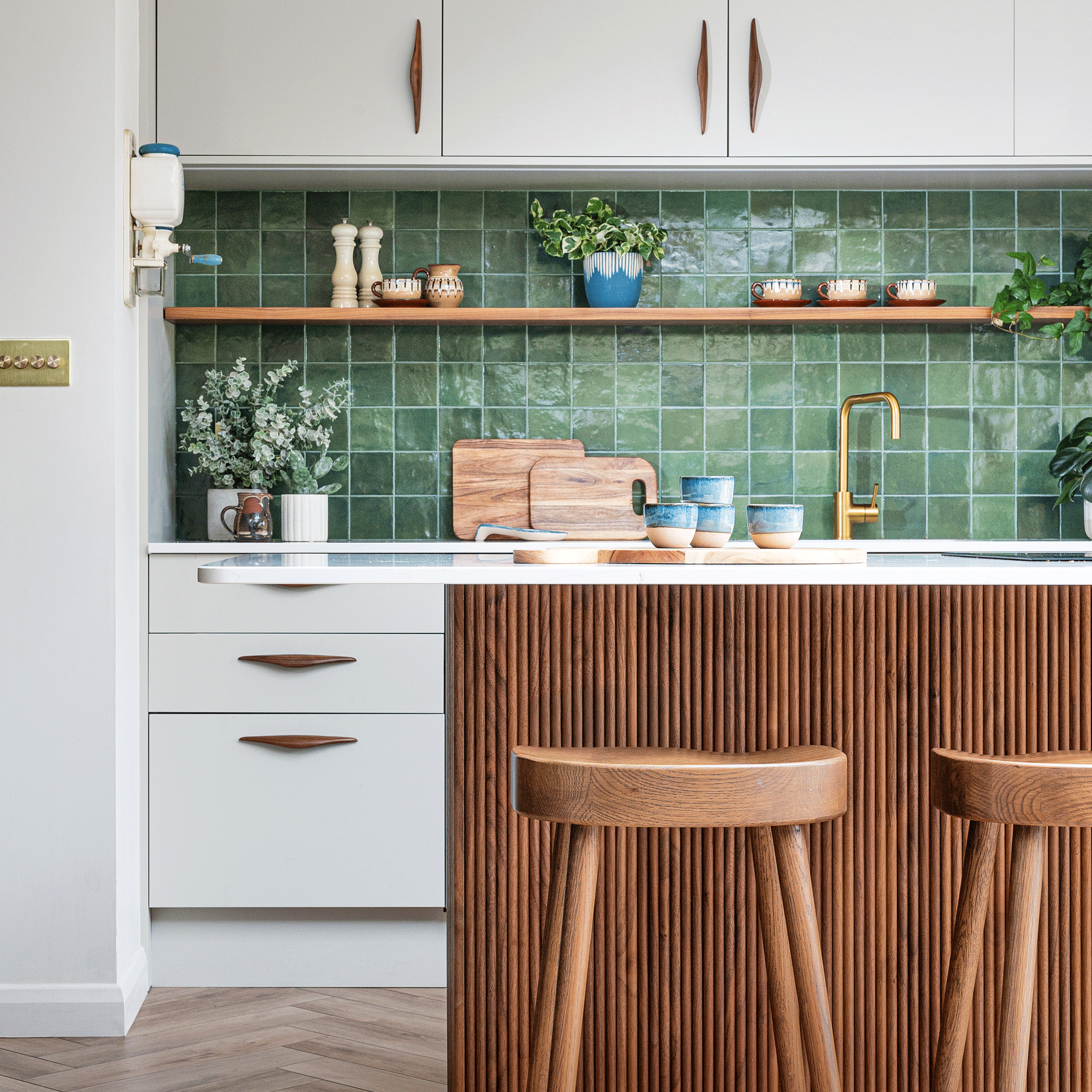 a kitchen with white cabinets, a green tiled splashback and a wooden fluted kitchen island and wooden bar stools