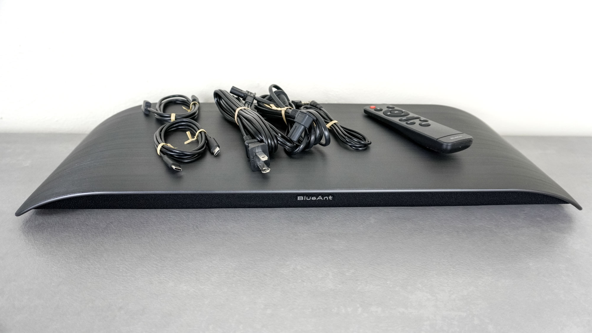 The BlueAnt Soundblade on a desk with all of the included cables and the remote on top of the soundbar