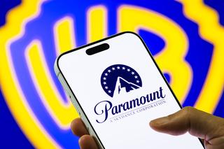 Shot of Warner Bros. logo behind a smart phone showing a Paramount logo.