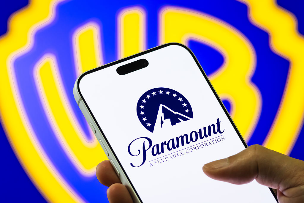 Shot of Warner Bros. logo behind a smart phone showing a Paramount logo.