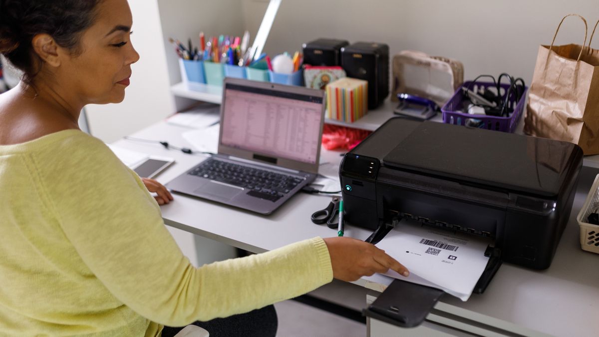 Woman sat at a desk, working from a laptop and printing a document using her printer