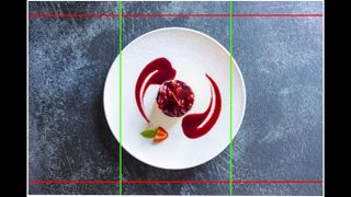 A food photo of a strawberry cheesecake on a white plate taken from above and against a dark textured background. There are lines overlaid on top of the image to show the different aspect ratios provided by Open Gate video recording