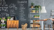 A kitchen diner with a very large, floor to ceiling chalkboard on onr wall with chalk cafe art and a shopping list