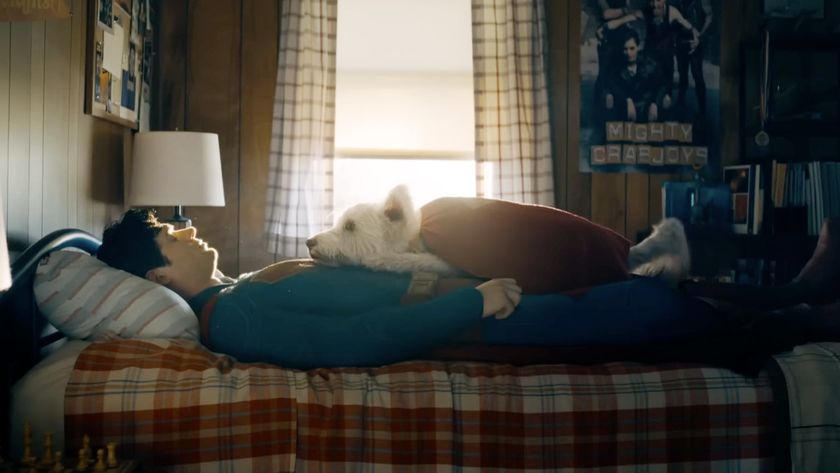Superman, played by David Corenswet, lies on the bed recouping with Krypto the superdog resting on his chest. 