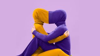 Two people sitting facing each other with the hoods of their tops connecting to obscure their faces