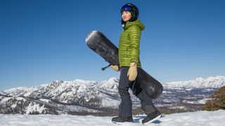 Woman walking wearing snowboarding helmet with board looking across the mountains