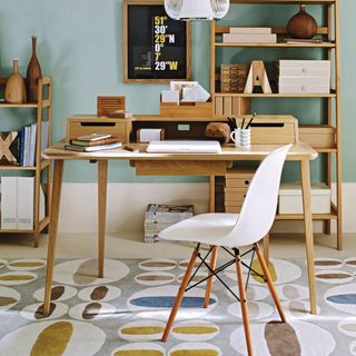 ight blue home office, fifties wooden desk, shelving unit and white plastic chair, white wire light shade, retro circle print pug, sunburst wall clock, framed print on wall, wooden vases.