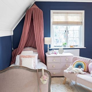 Child's bedroom with dark blue walls and a pink bed canopy, pink painted chest of drawers and pink furniture