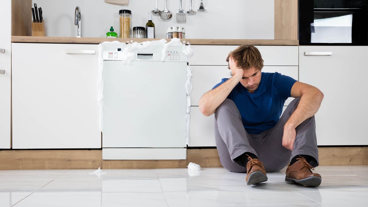 How to unclog a dishwasher: a man sitting in front of a blocked dishwasher