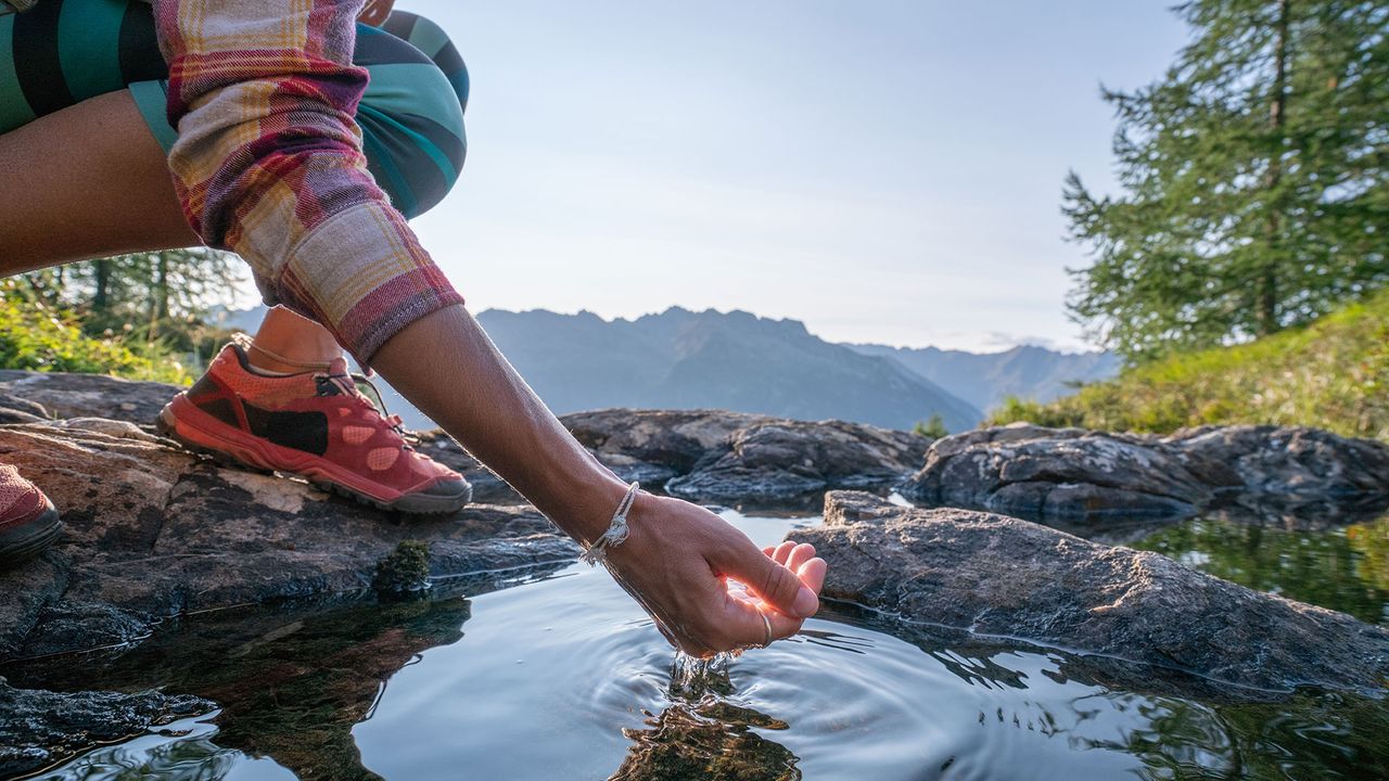 woman scooping mountain water from a pool