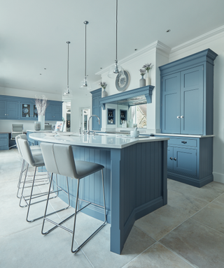 A Tom Howley blue kitchen with three lights over an island.
