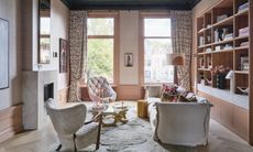 Pink living room with stone fireplace, linen sofa, cream armchair and patterned curtains