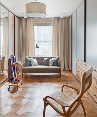 dressing room with parquet floor, mirrored wardrobes, neutral sofa and curved chair