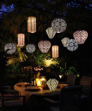 clusters of lanterns hung over an outdoor table lit up at night