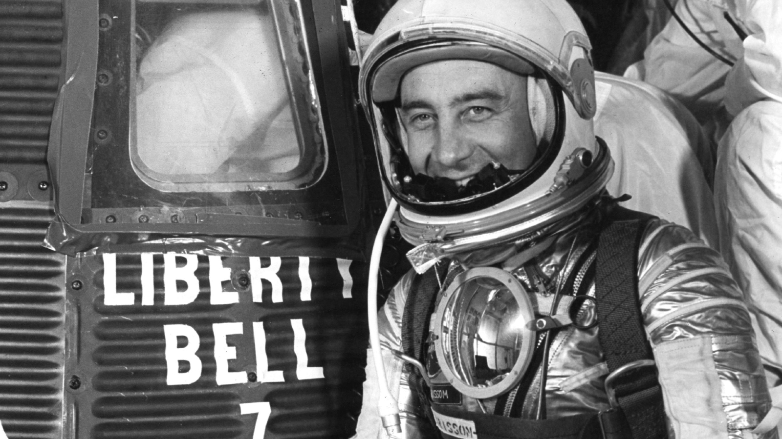 An astronaut wearing a spacesuit stands next to a large metal capsule labeled: 'Liberty Bell 7'