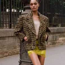 Model wearing a yellow lace skirt, off white top and a tweed blazer sold at net-a-porter