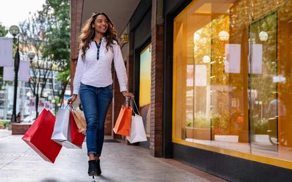 Woman holding red and silver shopping bags walks past a store window.