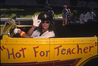 David Lee Roth in a yellow vintage car with "Hot For Teacher" painted on the side