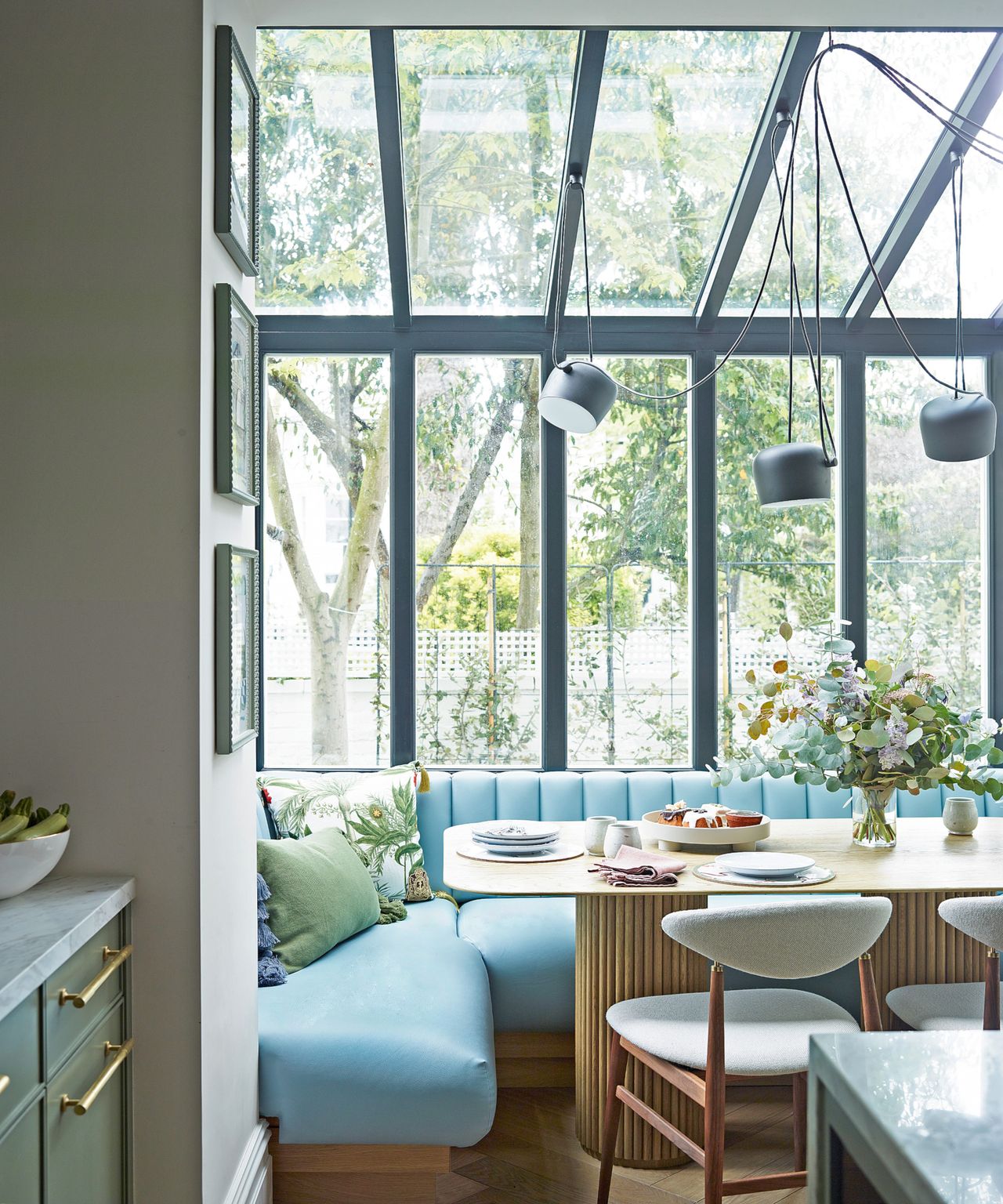 Dining area with metal framed windows, blue faux leather banquette, wooden dining table and Flos . pendant